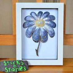 a blue flower in a white frame sitting on top of a table next to a rock