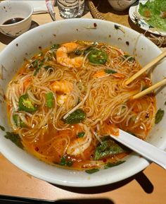 a white bowl filled with noodles and shrimp next to chopsticks on a table