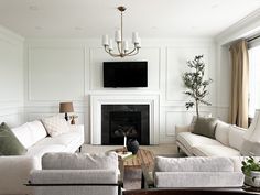 a living room filled with white furniture and a flat screen tv mounted above the fireplace