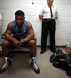 a man sitting on a bench in a locker room next to another man with boxing gloves