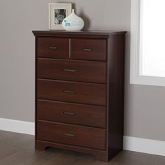 a wooden dresser sitting next to a window in a room with hardwood floors and gray walls