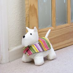 a small white dog with a scarf around its neck standing in front of a door