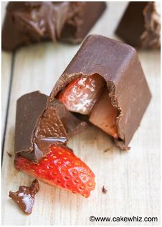 chocolate and strawberries are cut in half on a wooden table with one piece missing