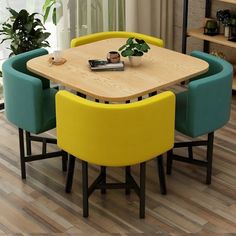 a wooden table surrounded by blue and yellow chairs in front of a window with potted plants