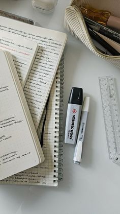 several notebooks and pens are sitting on a white table next to a measuring tape