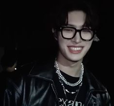 a young man wearing glasses and a black leather jacket is smiling at the camera in the dark