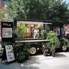 a food truck parked on the side of the road with plants in front of it