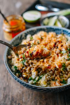 a bowl filled with rice and vegetables on top of a wooden table next to a spoon