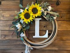 a sunflower wreath with the letter l hanging on a wooden wall next to a rope