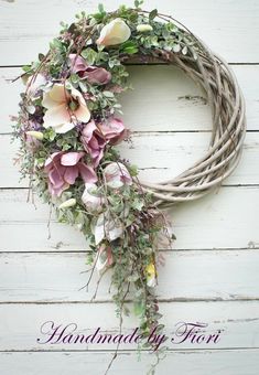 a wreath with pink flowers and greenery hanging on a white wooden wall that says handmade by floris