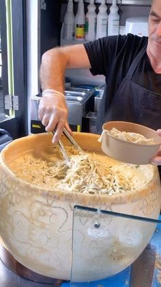 a man in an apron scooping noodles out of a large bowl