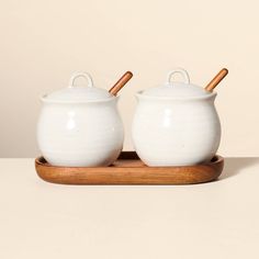 two white pots with wooden handles on a tray