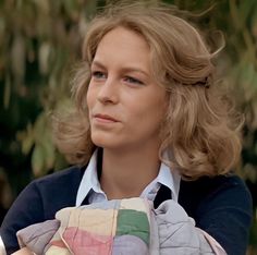 a woman holding a baby in her arms and looking off into the distance with trees in the background