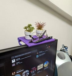 a computer monitor with glasses and a potted plant sitting on top of the screen