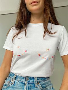 a woman wearing a white t - shirt with flowers on the chest and short sleeves