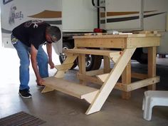 a man working on a wooden table in front of a rv parked in a garage