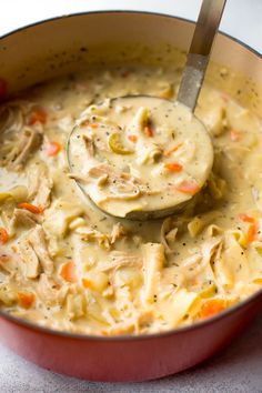 a ladle full of chicken noodle soup in a red pot