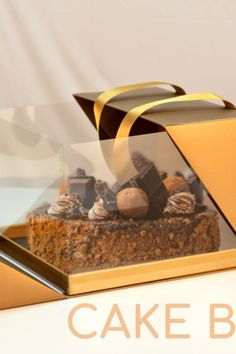 a cake in a glass box with gold ribbon around it and some nuts on top