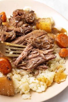 a white plate topped with meat, potatoes and carrots on top of mashed potatoes