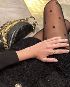 a woman's legs with black stockings and gold rings on them, while holding a purse