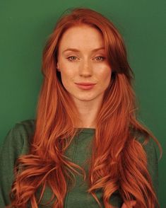 a woman with long red hair standing in front of a green wall and looking at the camera