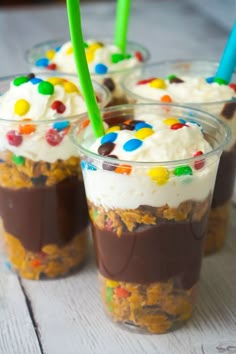 three cups filled with ice cream and toppings on top of a wooden table next to a green straw