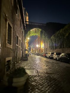 a cobblestone street at night with cars parked on the side and under an arch