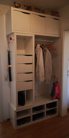 a white closet with clothes hanging on it's doors and shoes in the bottom drawer