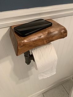 a wooden toilet paper holder with a cell phone on it's top shelf above the toilet