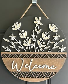 a welcome sign hanging from the side of a door with flowers and leaves on it