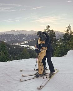 two skiers embracing each other on the top of a ski slope with mountains in the background