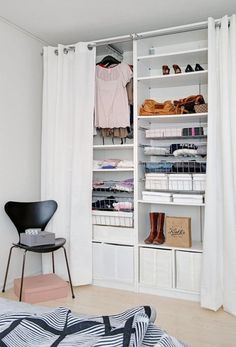 a white closet with clothes, shoes and bags on shelves next to a chair in front of a window