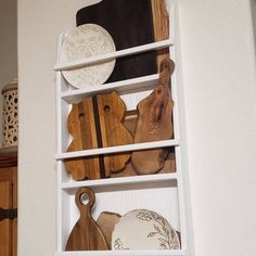 a shelf filled with wooden cutting boards on top of a white wall next to a cabinet