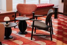 three chairs and two tables in a room with red carpeted flooring, one has a glass on the table