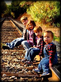 three children sitting on train tracks with their feet in the air and one child standing next to them