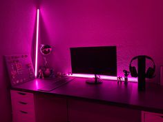 a desk with a computer monitor and headphones on it in front of a pink wall