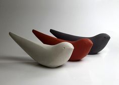 three different colored birds sitting next to each other on a white surface with one black, one red and one grey