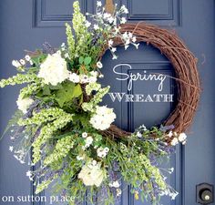 a wreath with white flowers and greenery hangs on a blue front door in the daytime