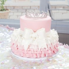 a pink and white cake with a tiara on top is sitting on a table