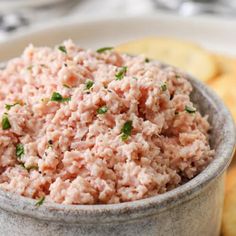 a close up of a bowl of food with crackers in the background on a table