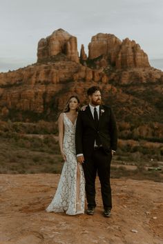 a bride and groom standing on top of a mountain in front of the red rocks