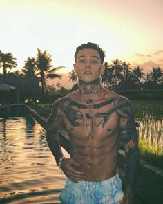 a man standing in front of a body of water with tattoos on his chest and arms