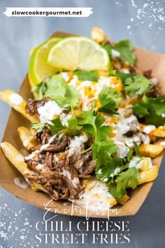 mexican food with meat, cheese and cilantro on a paper tray next to lime wedges