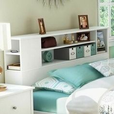 a white bed sitting under a window next to a shelf filled with pictures and other items