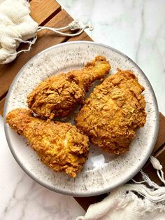 three fried chicken on a white plate next to a cloth bag and some garlic flakes