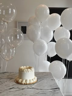 a cake with white frosting and balloons in the air on a marble countertop