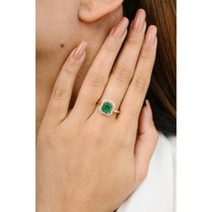 a woman's hand holding an emerald and diamond ring in front of her face