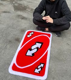 a man sitting on the ground next to a red and white rug that has arrows in it