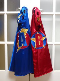 two children's capes hanging from hooks on a white door with glass panes in the background