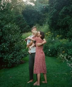 a man and woman standing in the grass with a child on their shoulders, both holding each other